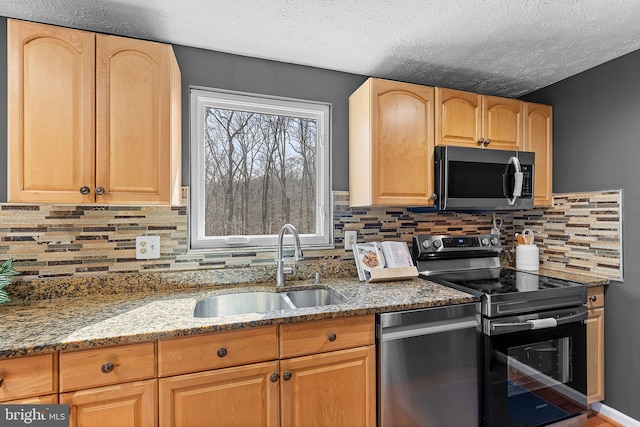 kitchen with backsplash, light brown cabinetry, light stone counters, appliances with stainless steel finishes, and a sink