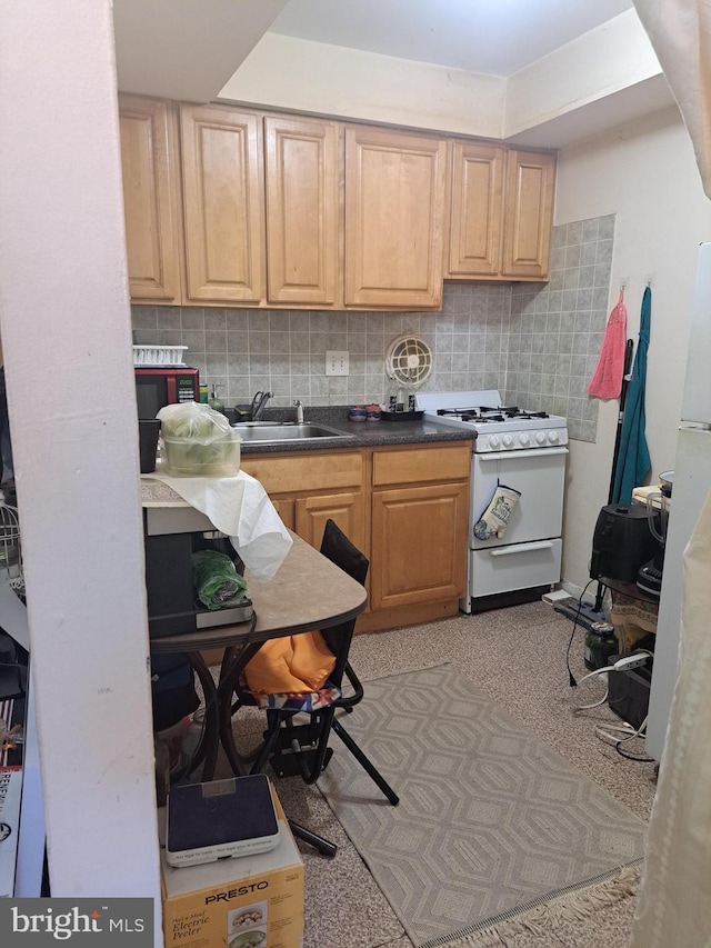 kitchen featuring dark countertops, light brown cabinetry, white gas range oven, decorative backsplash, and a sink