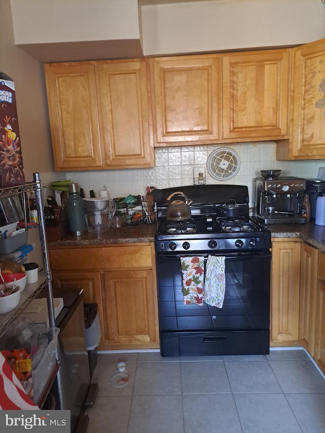 kitchen with tile patterned floors, backsplash, black range with gas stovetop, and dark stone countertops