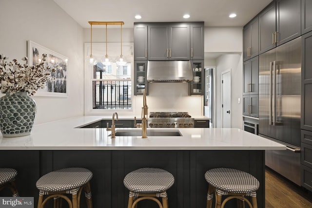 kitchen with under cabinet range hood, a breakfast bar, built in refrigerator, a sink, and light stone countertops