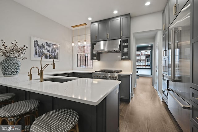 kitchen featuring dark wood finished floors, a breakfast bar area, a sink, a peninsula, and under cabinet range hood