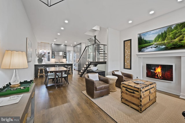 living area featuring recessed lighting, a warm lit fireplace, stairway, and wood finished floors