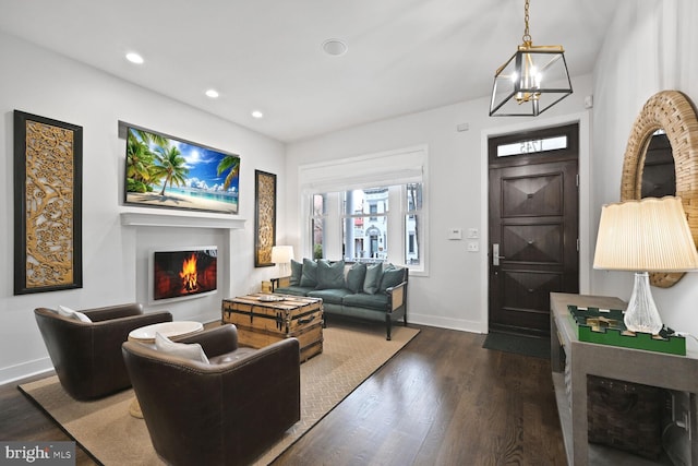 entrance foyer with baseboards, dark wood-type flooring, a lit fireplace, a notable chandelier, and recessed lighting