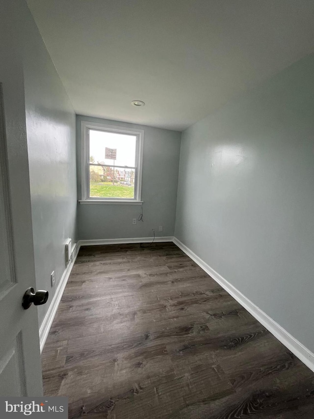 empty room with dark wood-style floors, visible vents, and baseboards