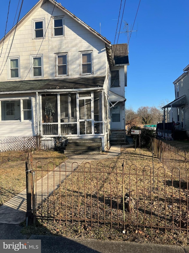 rear view of house featuring entry steps, a sunroom, and a fenced front yard