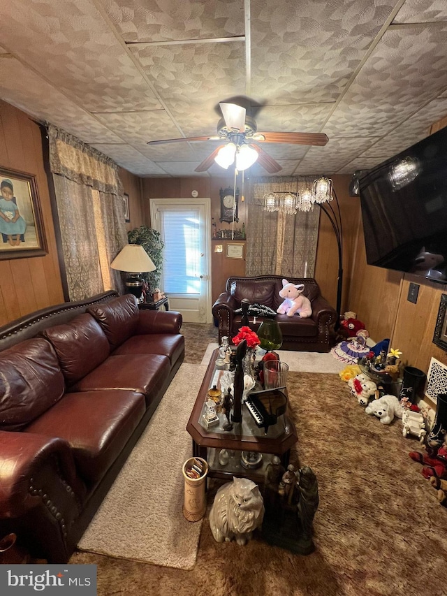 living area with ceiling fan, carpet, and wooden walls