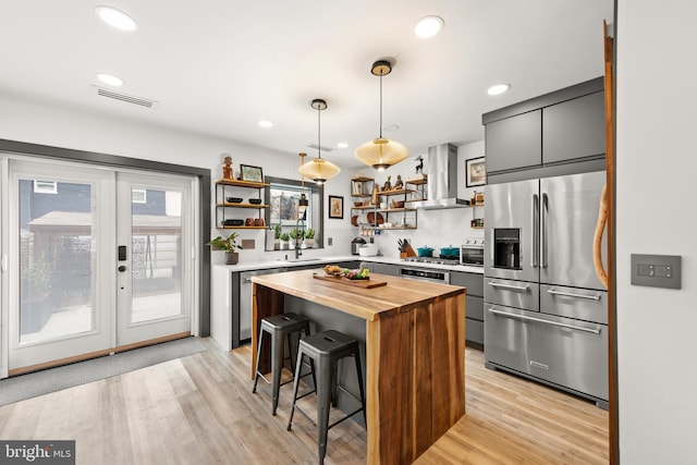kitchen featuring open shelves, appliances with stainless steel finishes, a breakfast bar, wooden counters, and wall chimney exhaust hood