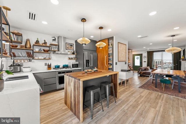 kitchen featuring open shelves, a sink, wood counters, wall chimney exhaust hood, and stainless steel appliances