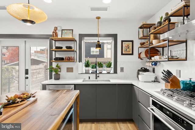 kitchen featuring stainless steel appliances, open shelves, gray cabinetry, and a sink