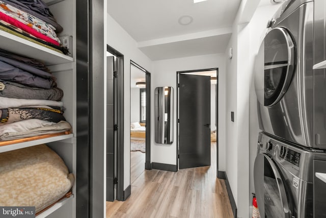 laundry area with light wood-type flooring, laundry area, baseboards, and stacked washing maching and dryer