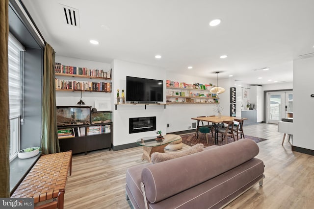 living area featuring recessed lighting, visible vents, a glass covered fireplace, and light wood finished floors