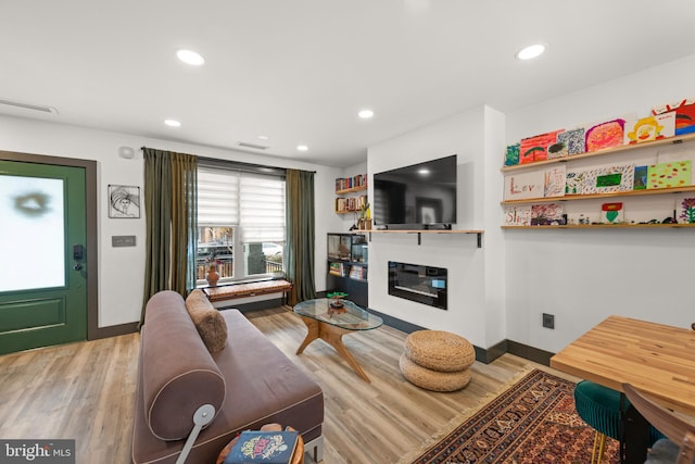 living room featuring a glass covered fireplace, recessed lighting, light wood finished floors, and visible vents