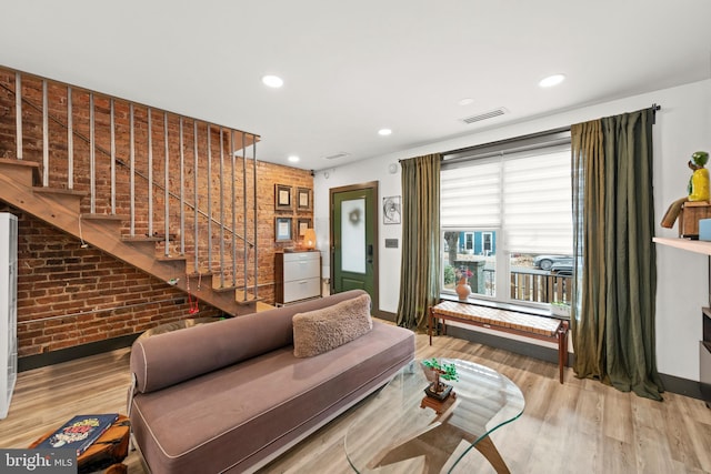 living area with visible vents, baseboards, wood finished floors, and brick wall