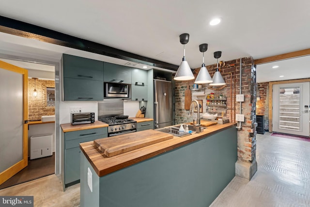 kitchen featuring stainless steel appliances, brick wall, wooden counters, and a sink