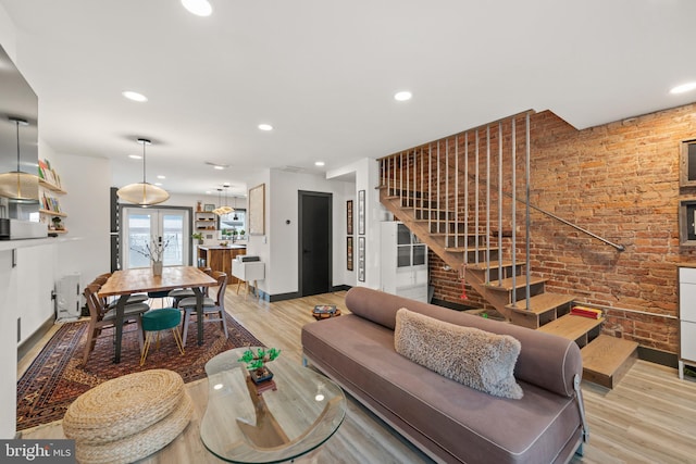 living area with stairs, brick wall, baseboards, and light wood-style flooring