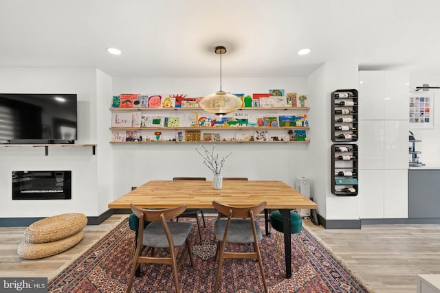 dining space featuring a glass covered fireplace, baseboards, recessed lighting, and light wood-style flooring