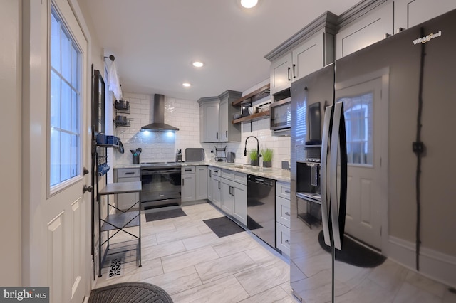 kitchen featuring open shelves, gray cabinetry, a sink, wall chimney range hood, and black appliances