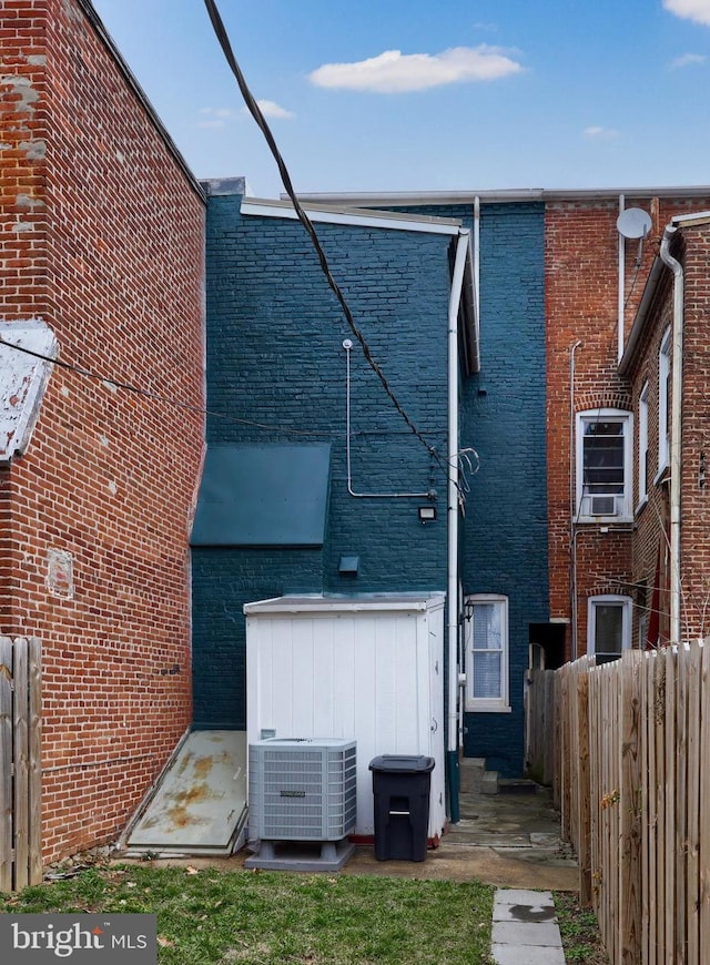 rear view of property featuring central AC unit, fence, and brick siding