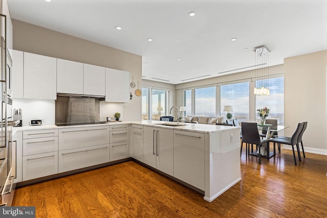 kitchen featuring black electric cooktop, a peninsula, a sink, white cabinets, and light countertops