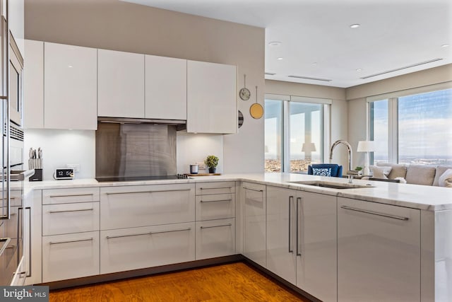 kitchen with light countertops, a peninsula, a sink, and white cabinetry