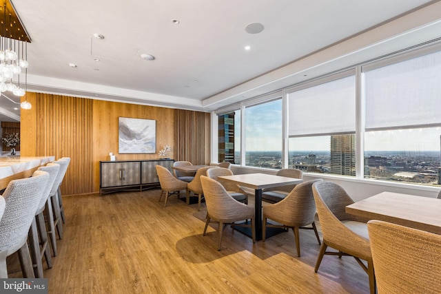 dining area with light wood-style floors, a notable chandelier, wooden walls, and a city view