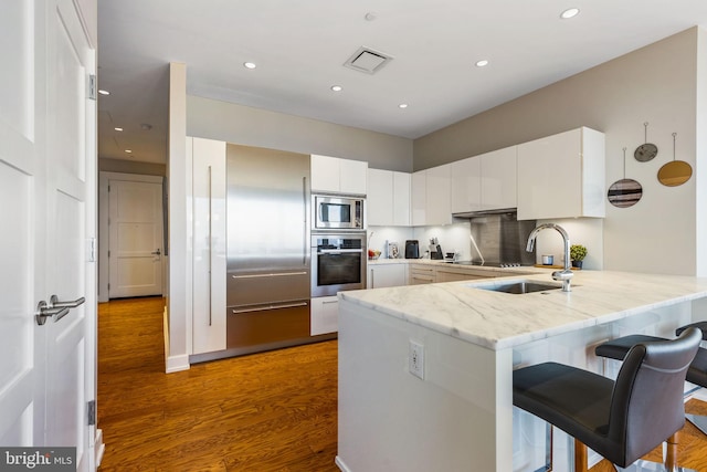 kitchen featuring stainless steel appliances, a peninsula, a sink, white cabinets, and dark wood-style floors