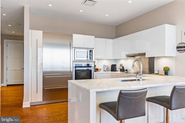 kitchen featuring stainless steel appliances, visible vents, light wood-style flooring, white cabinets, and a peninsula