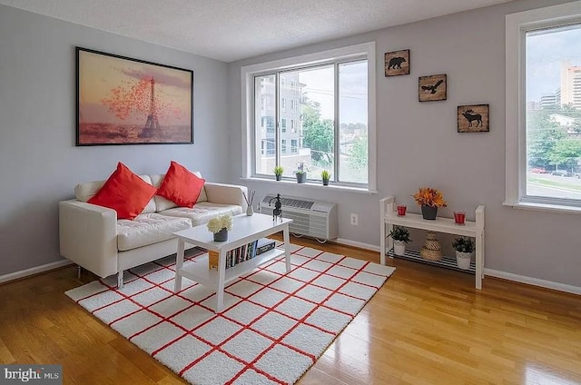 living area with a textured ceiling, an AC wall unit, light wood-type flooring, and baseboards