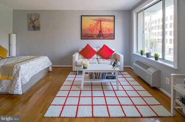 bedroom featuring a wall mounted AC, baseboards, and wood finished floors