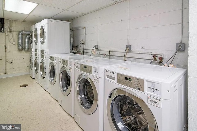 common laundry area featuring concrete block wall, light floors, stacked washer / drying machine, and independent washer and dryer