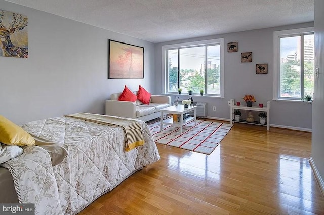 bedroom with a textured ceiling, multiple windows, baseboards, and wood finished floors