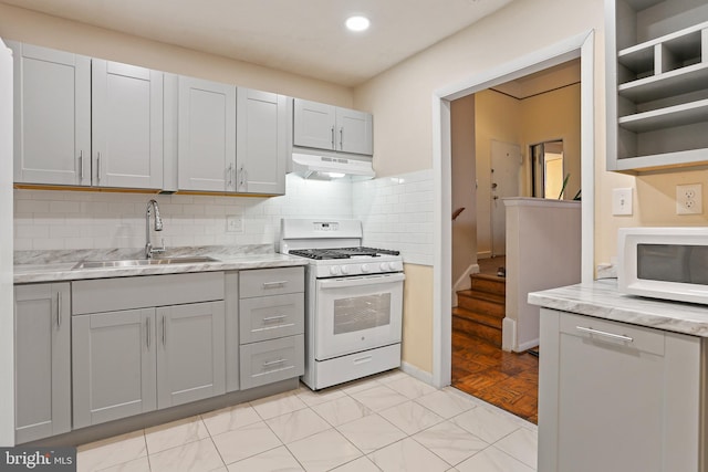 kitchen featuring gray cabinets, backsplash, a sink, white appliances, and under cabinet range hood