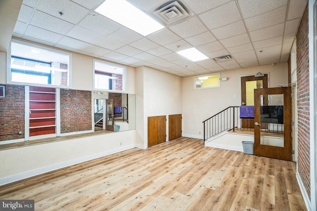 spare room featuring brick wall, a paneled ceiling, wood finished floors, and visible vents