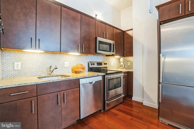 kitchen featuring tasteful backsplash, dark wood finished floors, light stone counters, appliances with stainless steel finishes, and a sink