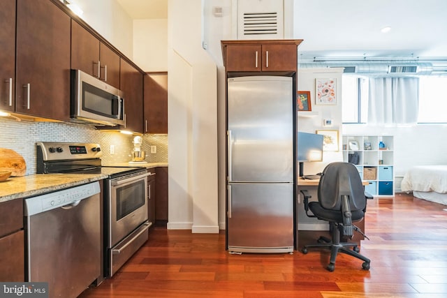 kitchen with dark brown cabinetry, decorative backsplash, dark wood-style floors, light stone countertops, and stainless steel appliances