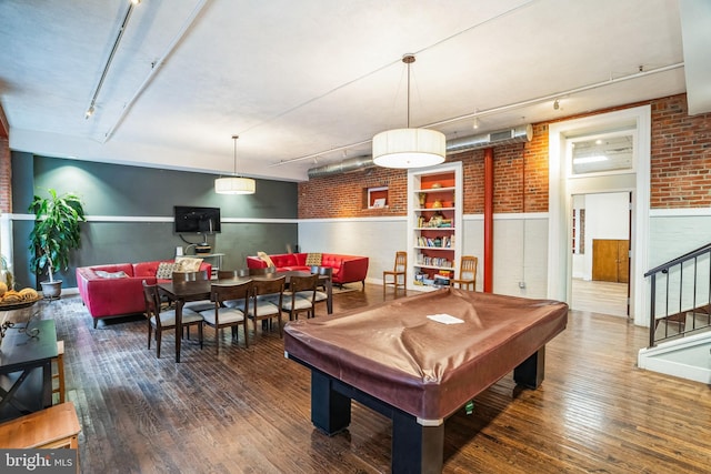 recreation room featuring track lighting, a wainscoted wall, brick wall, and wood finished floors