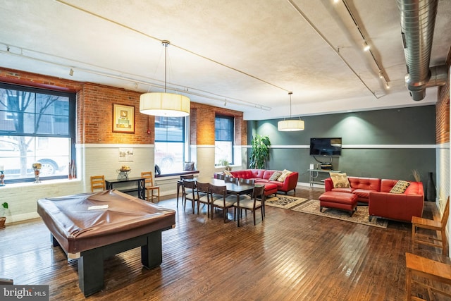 game room with a wainscoted wall, brick wall, hardwood / wood-style flooring, and track lighting