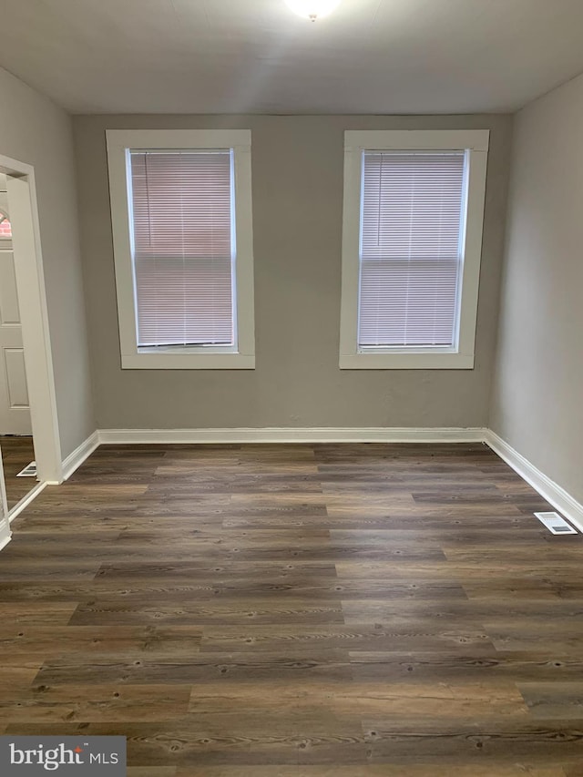 empty room with visible vents, baseboards, and dark wood finished floors