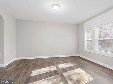 empty room with baseboards, arched walkways, and dark wood-style flooring