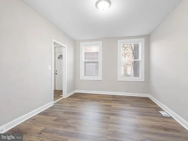 spare room with dark wood-style floors, lofted ceiling, visible vents, and baseboards