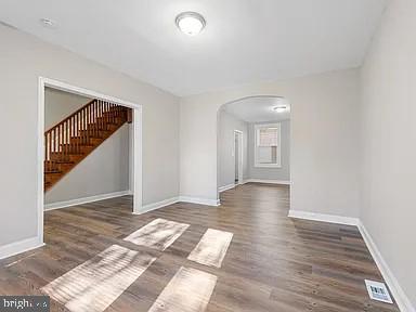 empty room with dark wood-style floors, arched walkways, visible vents, and baseboards