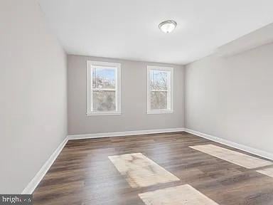 unfurnished room featuring baseboards and dark wood-style flooring