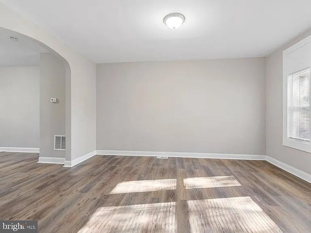 unfurnished room with arched walkways, dark wood-style flooring, visible vents, and baseboards