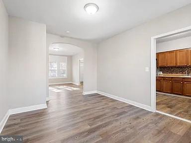 unfurnished dining area with baseboards, arched walkways, and wood finished floors