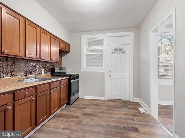 kitchen with a sink, light countertops, light wood-type flooring, brown cabinets, and gas stove