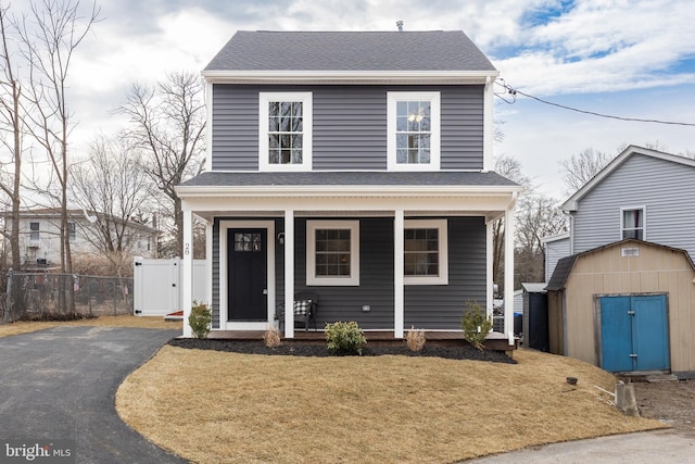 view of front of property with aphalt driveway, a shingled roof, an outdoor structure, a storage unit, and a front yard