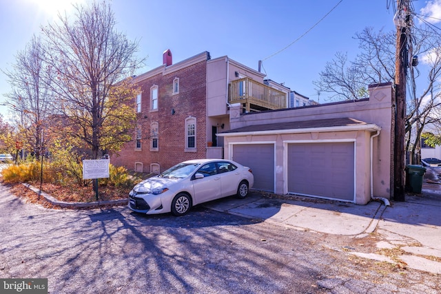 view of side of property featuring brick siding, a chimney, an attached garage, a balcony, and driveway