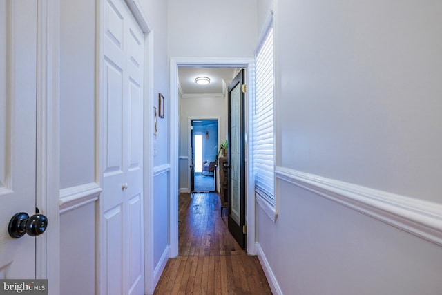 hallway with dark wood-type flooring, crown molding, and baseboards