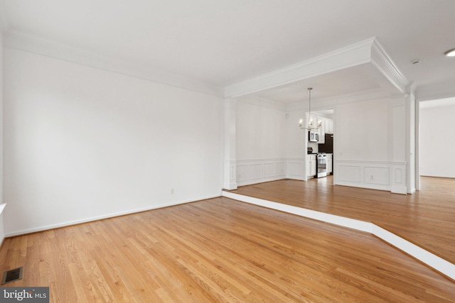 empty room with visible vents, light wood-style flooring, an inviting chandelier, crown molding, and a decorative wall