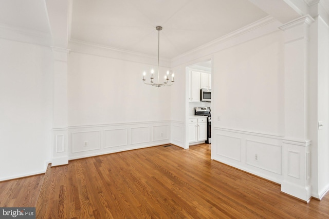 unfurnished dining area with ornamental molding, wood finished floors, an inviting chandelier, and decorative columns